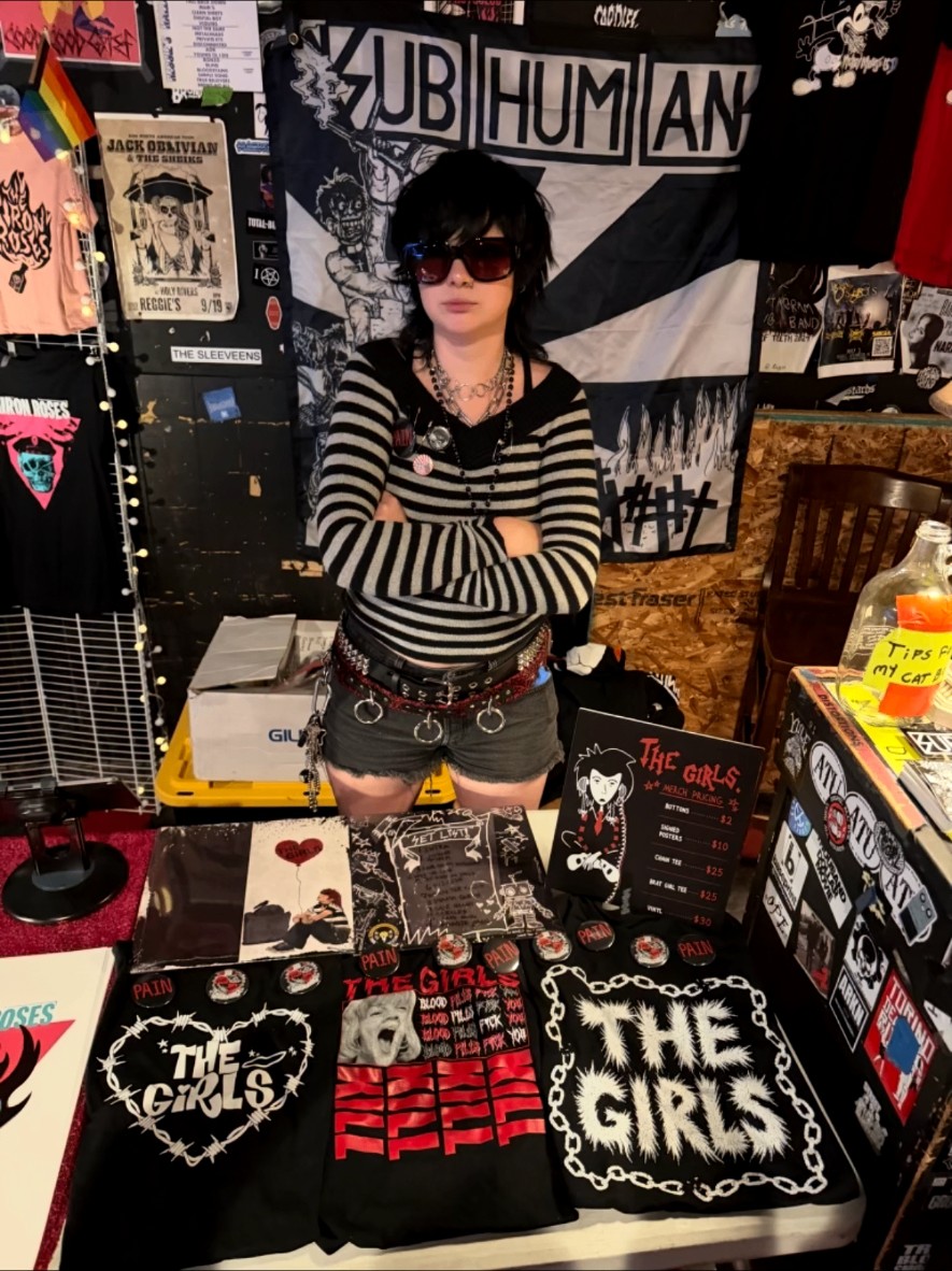 The Girls merch table with shirts, patches and buttons